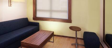 Una habitación con un sofá, una mesa de madera, una mesita redonda y una ventana con persianas.
