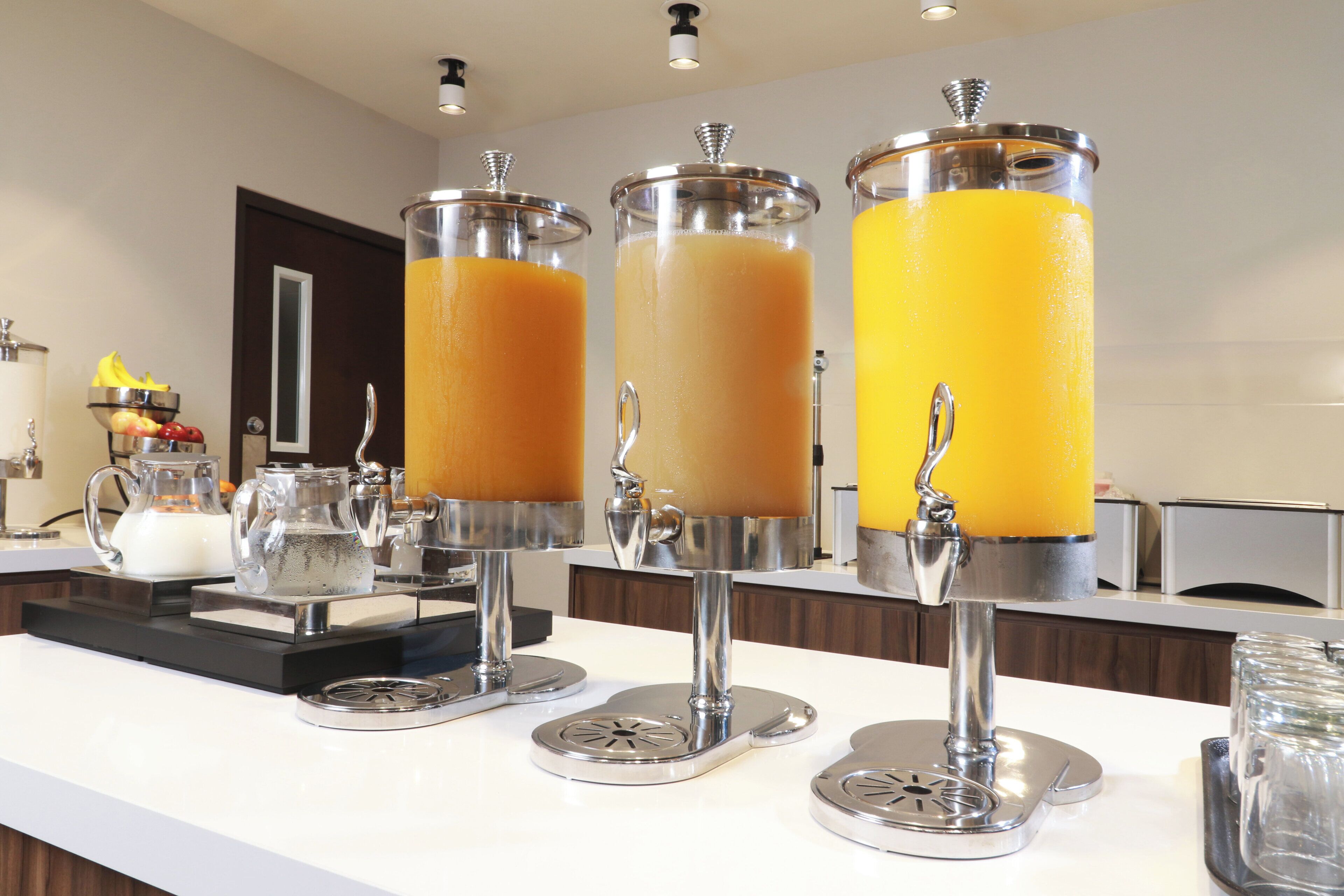 A juice bar with three dispensers filled with orange juice.