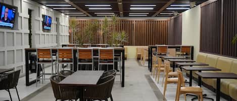 A modern indoor dining area with multiple tables and chairs, wooden panel walls, and ceiling lights.