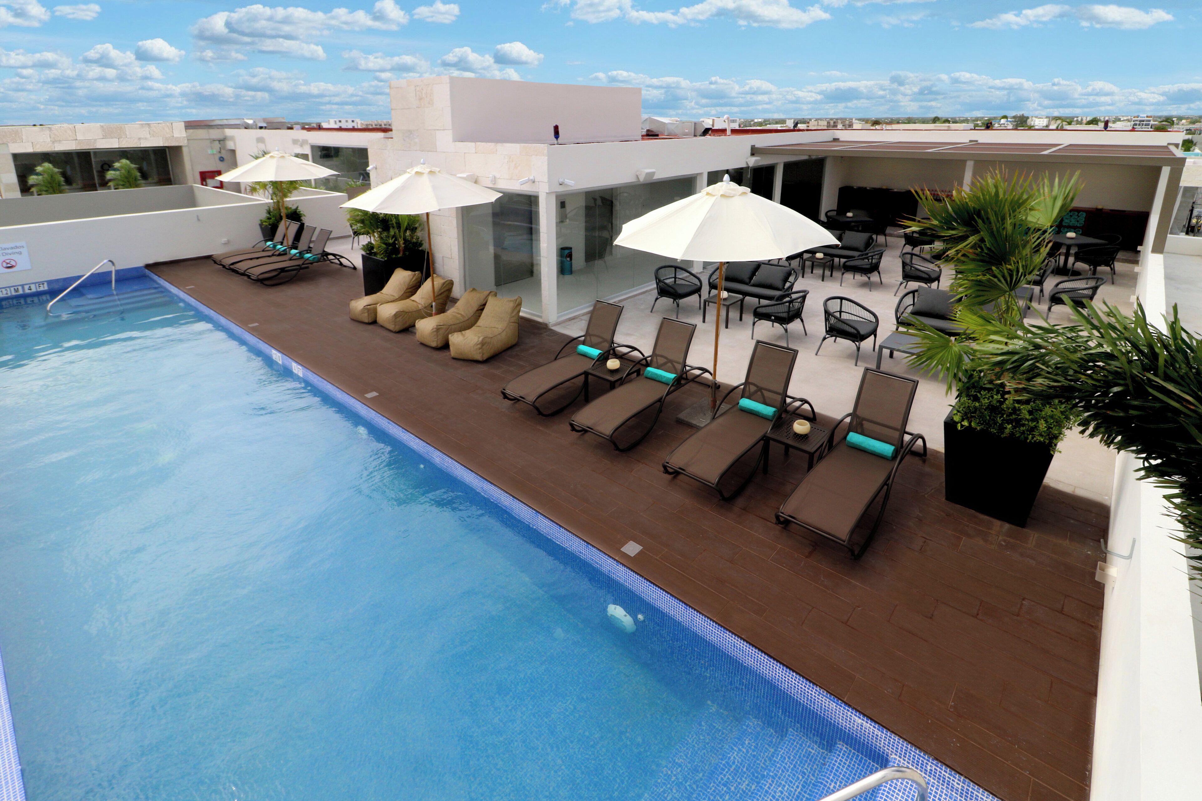 A rooftop pool area with sun loungers, umbrellas, and a view of the cityscape.