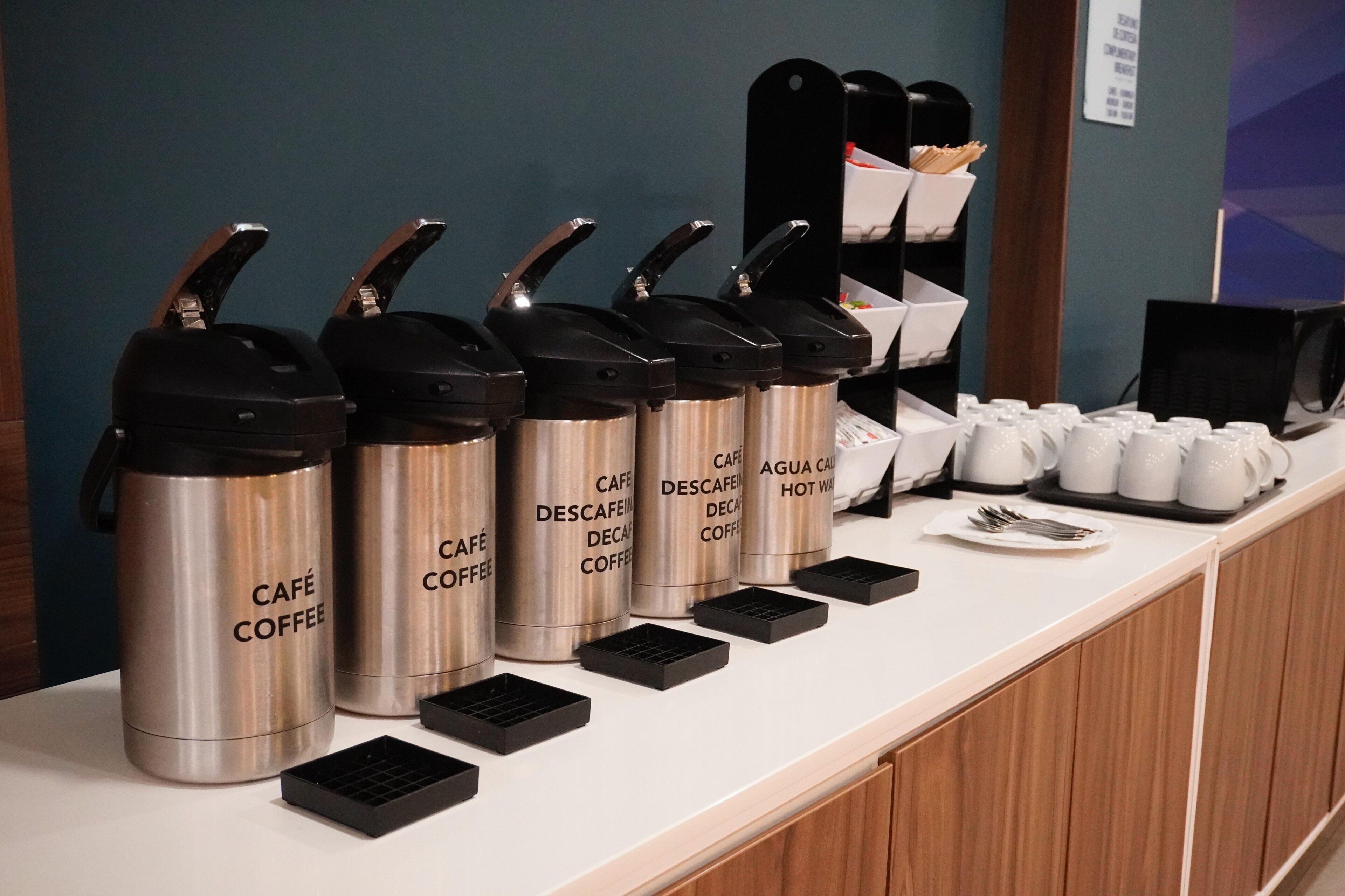 A coffee station with multiple coffee dispensers labeled 'CAFE COFFEE' and 'CAFE DESCAFE' on a counter.