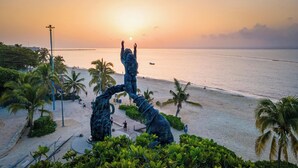 A beach with a sculpture, palm trees, and a sunset. - Holiday Inn Express & Suites Playa Del Carmen by IHG (Playa del Carmen)