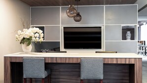 A modern kitchen with a large TV, two bar stools, and a vase of white flowers. - Holiday Inn Express & Suites Playa Del Carmen by IHG (Playa del Carmen)