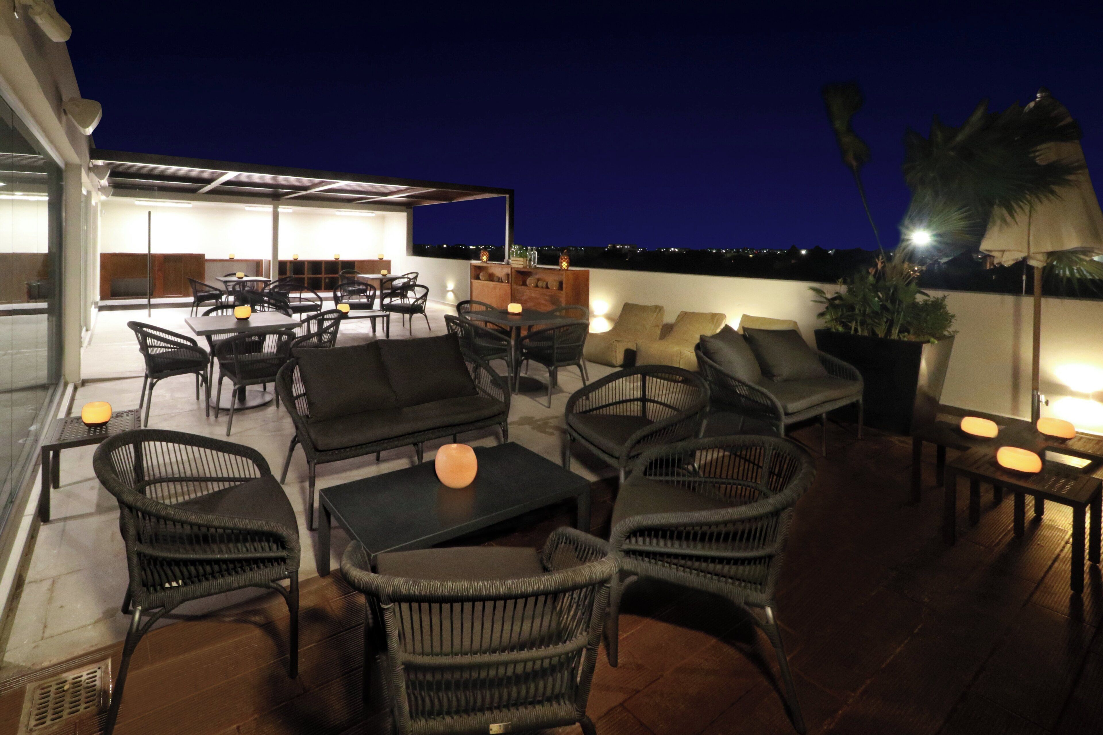 An outdoor seating area with wicker furniture, tables, and chairs, and a view of the city at night.