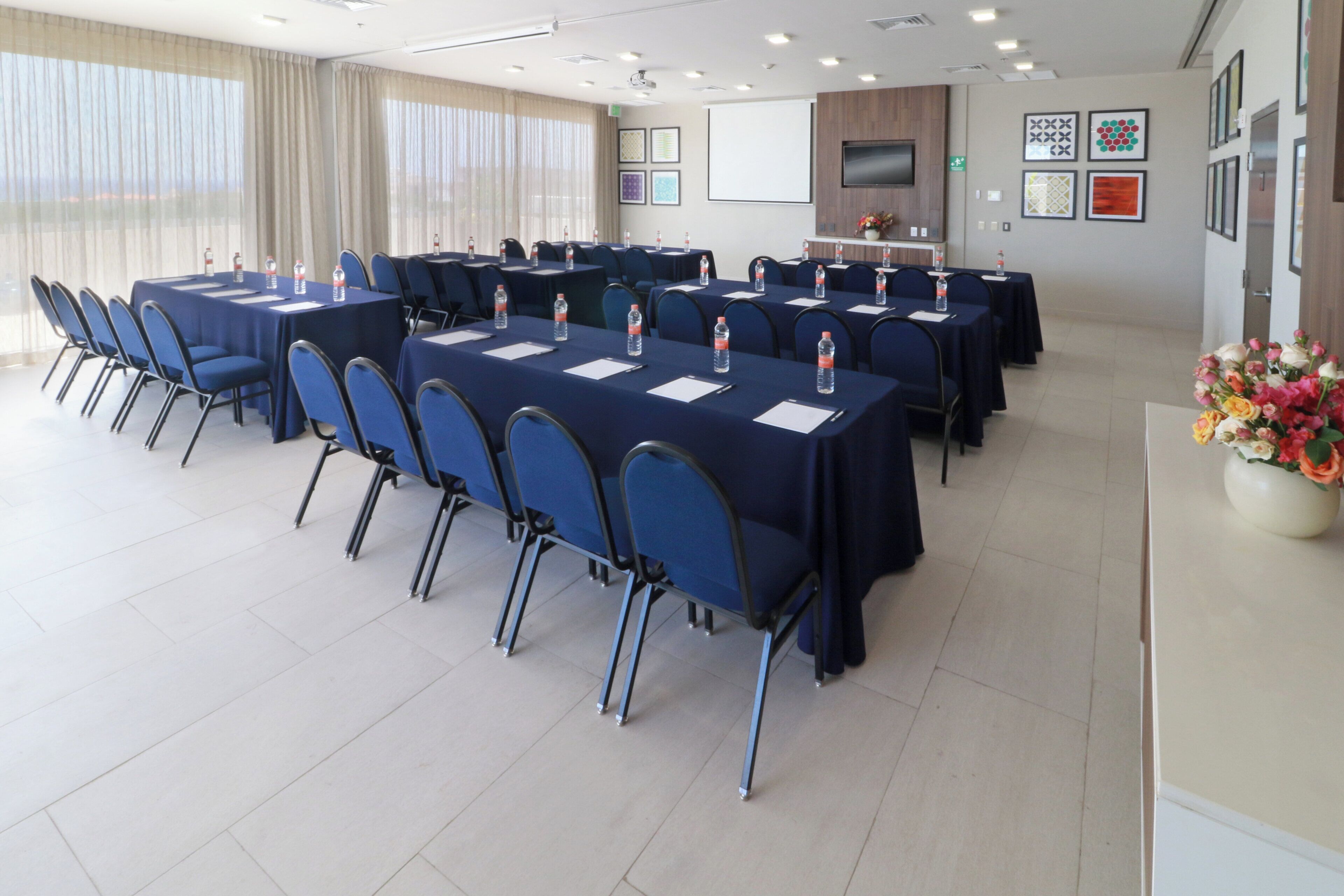 A conference room with multiple tables and chairs, water bottles on each table, and a large window with curtains.