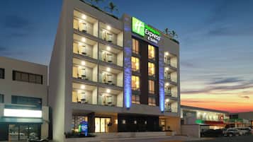 A multi-story hotel with a prominent Holiday Inn Express sign, balconies with seating, and a parking area with vehicles.