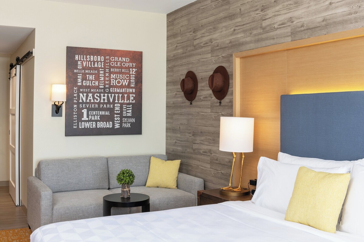 Ein Hotelzimmer mit einem großen Bett, einem grauen Sofa, einem kleinen Tisch mit Pflanze und einer Wand mit einer Wandkunst aus Wortwolken.