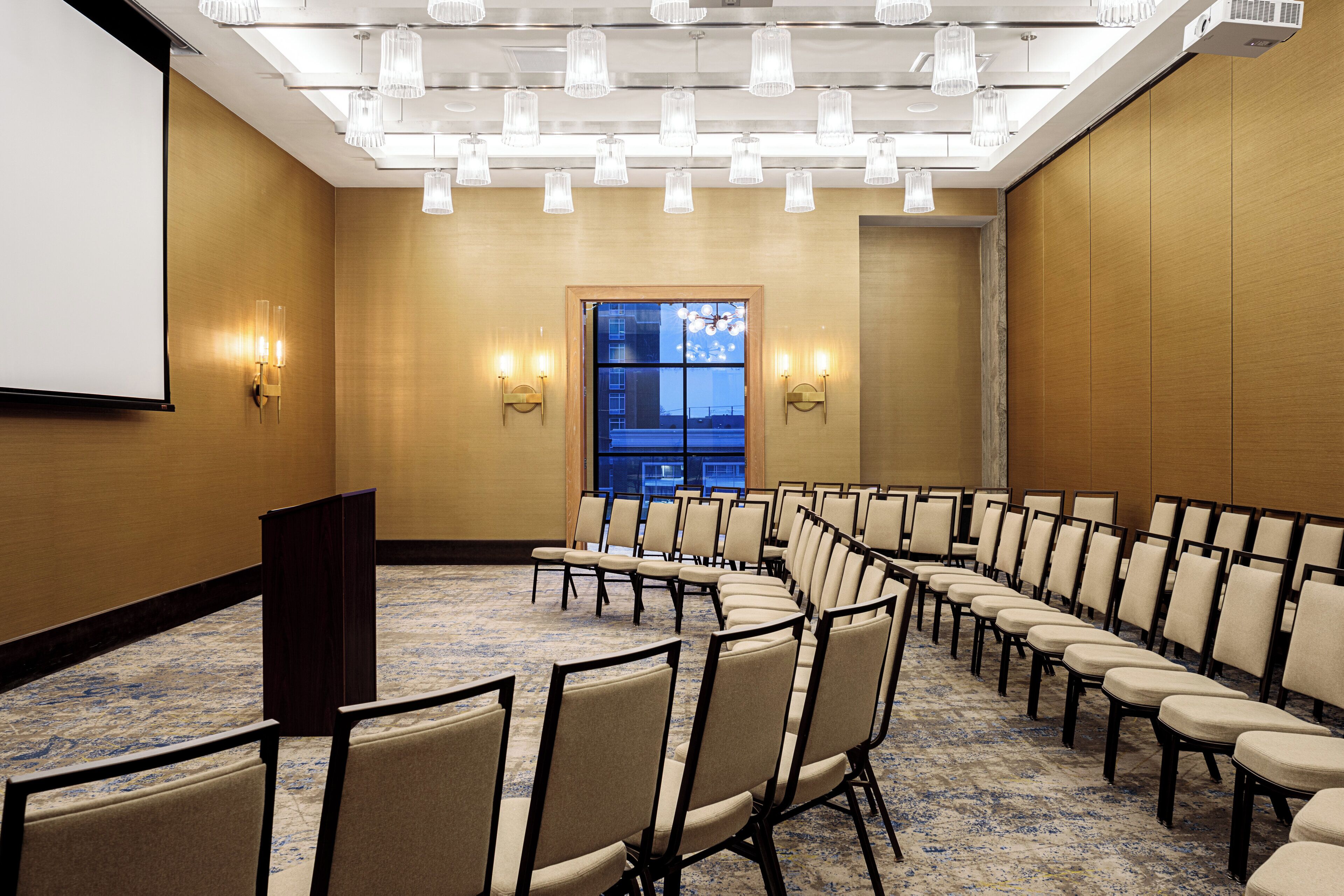 A conference room with rows of chairs, a podium, and wall-mounted lights.