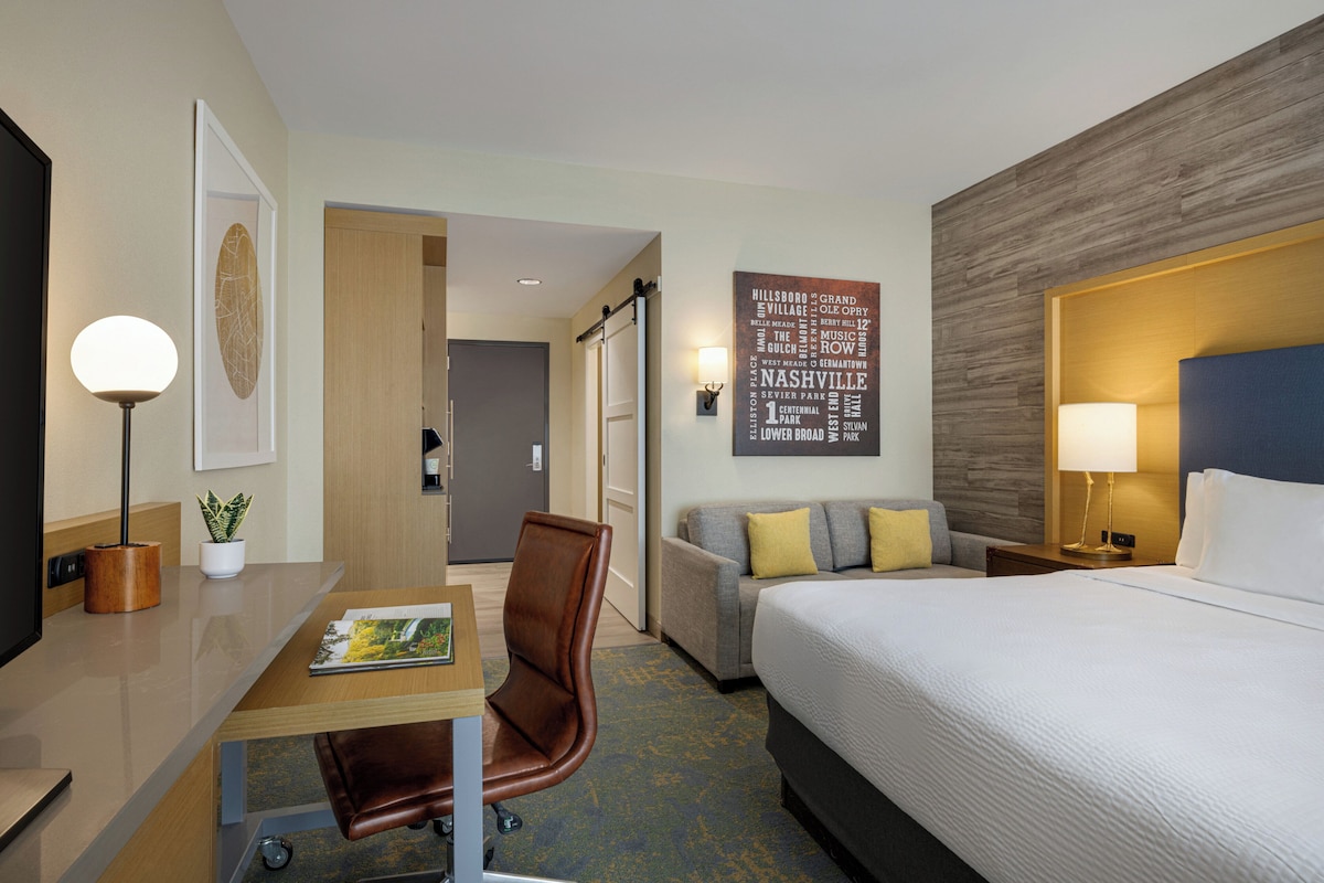 A hotel room with a bed, desk, chair, and a wall with a word cloud.