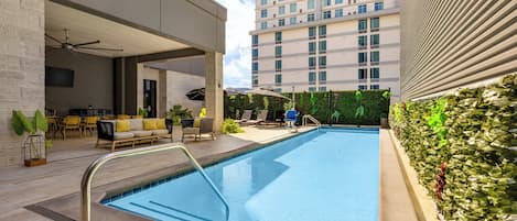 A modern indoor pool area with a clear pool, lounge chairs, and a high-rise building in the background.