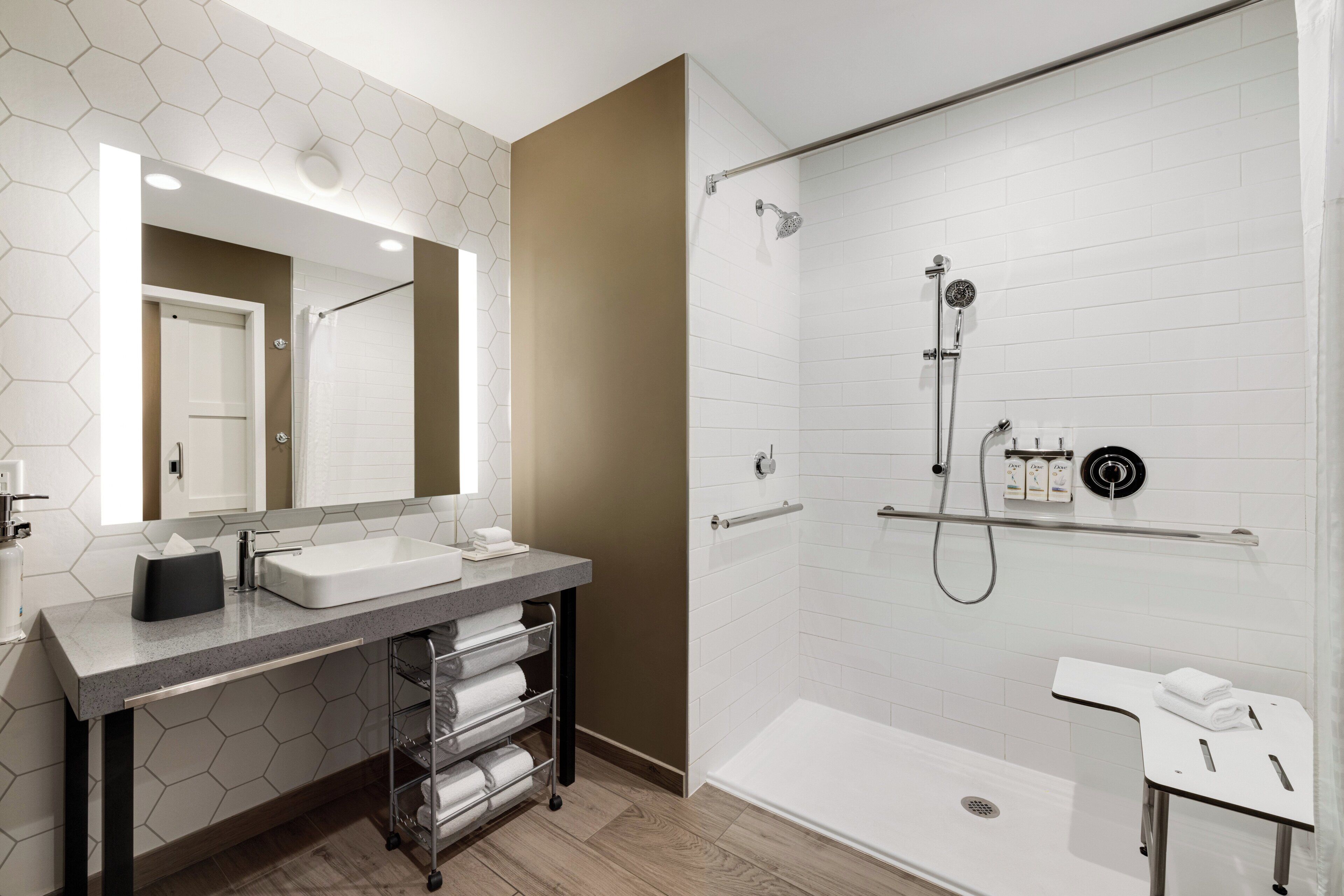 Un baño moderno con dos lavamanos, un espejo grande, una ducha con cabezal de ducha manual y un estante de vidrio.