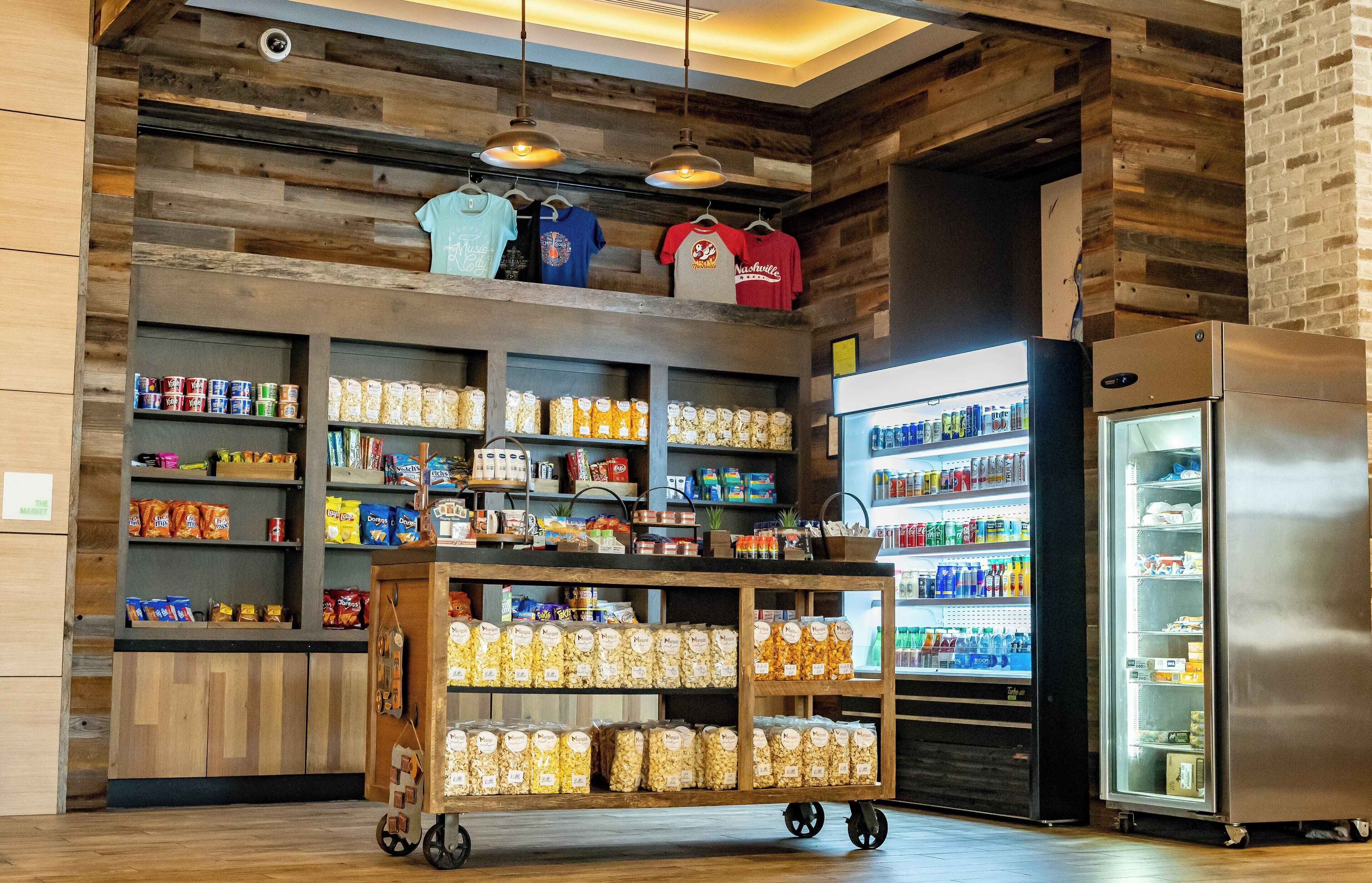 A snack bar with shelves stocked with various snacks, a refrigerated display case, and a cart with packaged goods.