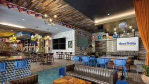 Eine moderne Bar mit Ledersitzgelegenheiten, einer Bar und einem großen Bildschirm, der "Almost Friday Sporting Club" zeigt.