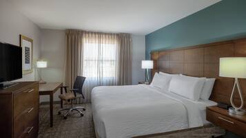 A hotel room with a bed, a desk, a chair, a TV, and a lamp.