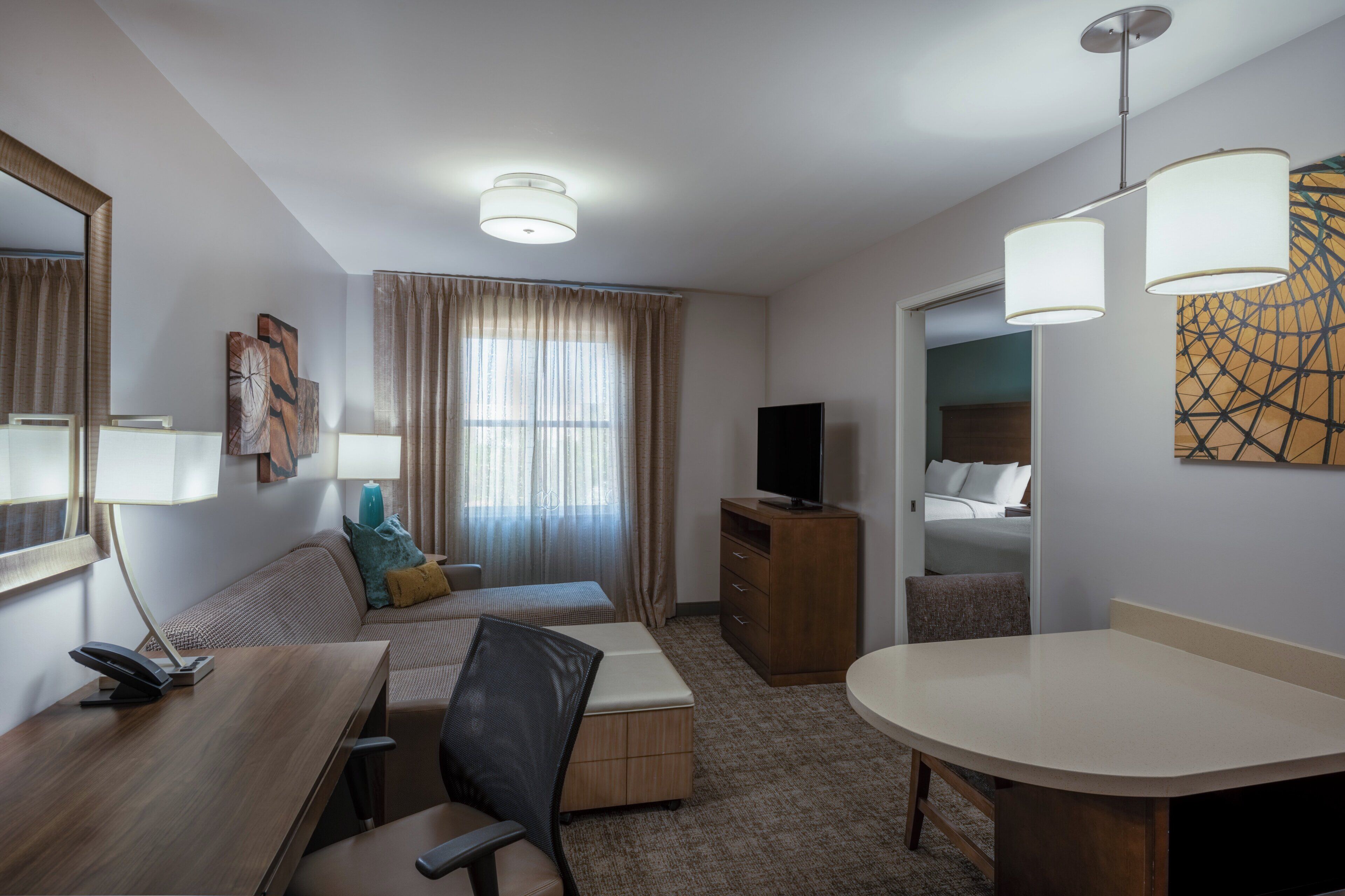 Habitación de hotel con cama, escritorio con silla, televisión y mesa de comedor.