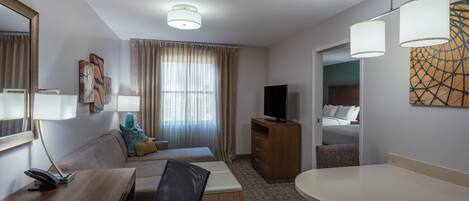 Habitación de hotel con cama, escritorio con silla, televisión y mesa de comedor.