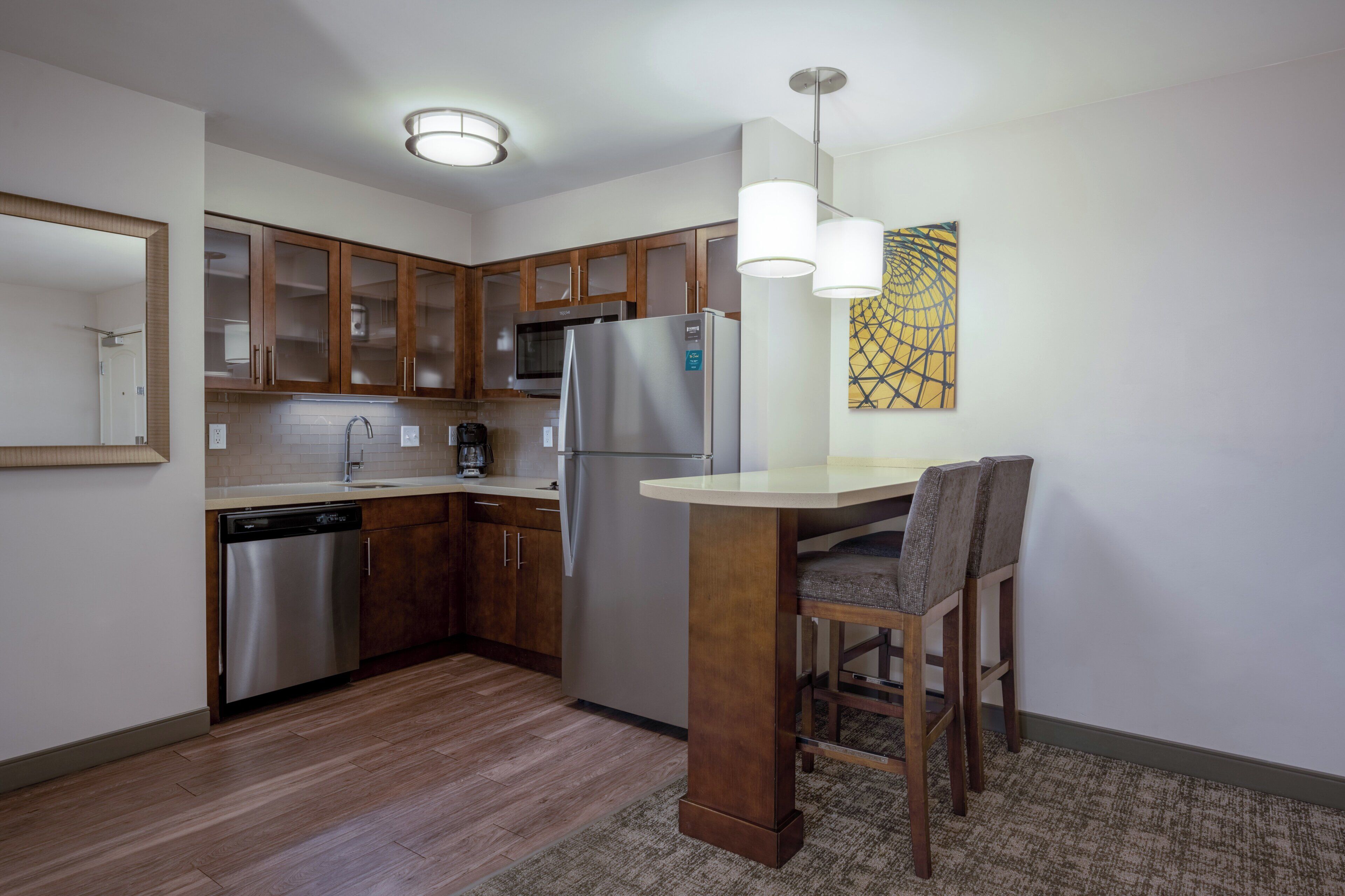 A compact kitchen with wooden cabinets, stainless steel appliances, and a small dining area with a chair.