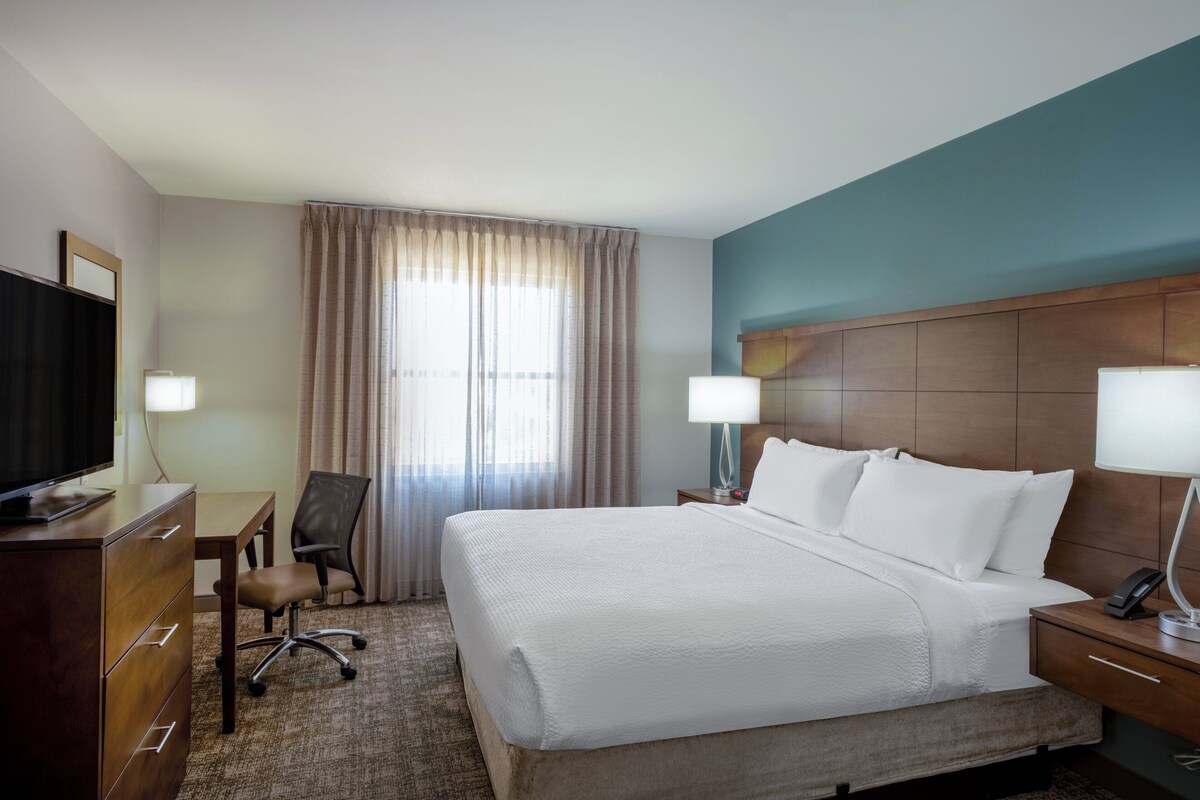 A hotel room with a large bed, a desk, a chair, a television, and two bedside lamps.