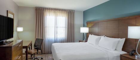 Habitación de hotel con una cama grande, un escritorio, una silla, un televisor y dos lámparas de noche.
