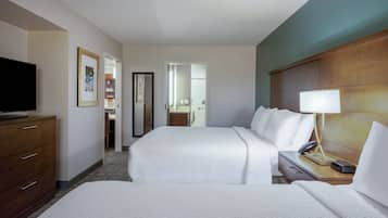 Una habitación de hotel con dos camas, televisión, mesita de noche con lámpara y cabecero de madera.