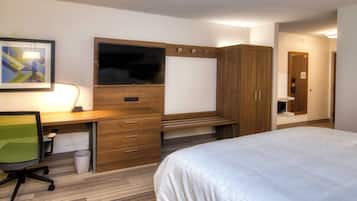 Una habitación de hotel con una cama, un escritorio con una silla, un televisor y un armario.