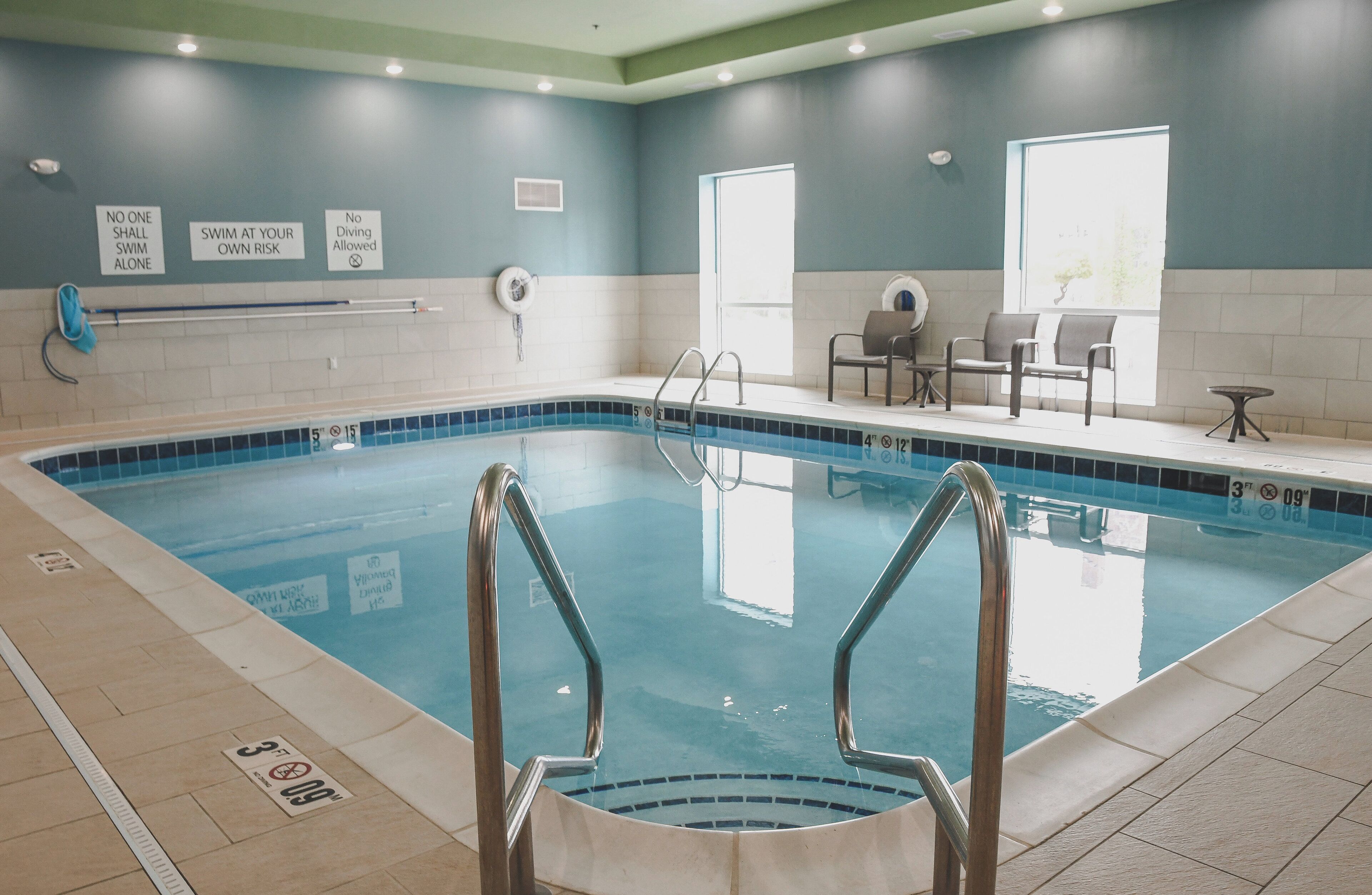 An indoor swimming pool with safety signs, a lifeguard chair, and a seating area with chairs and a table.