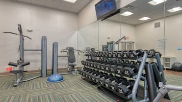 Ett gym med träningsutrustning, en tv-skärm och en utrymningsskylt.