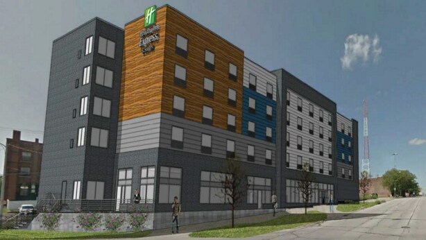A modern hotel with a flat roof, a prominent green and white logo, and a mix of window styles on the facade.