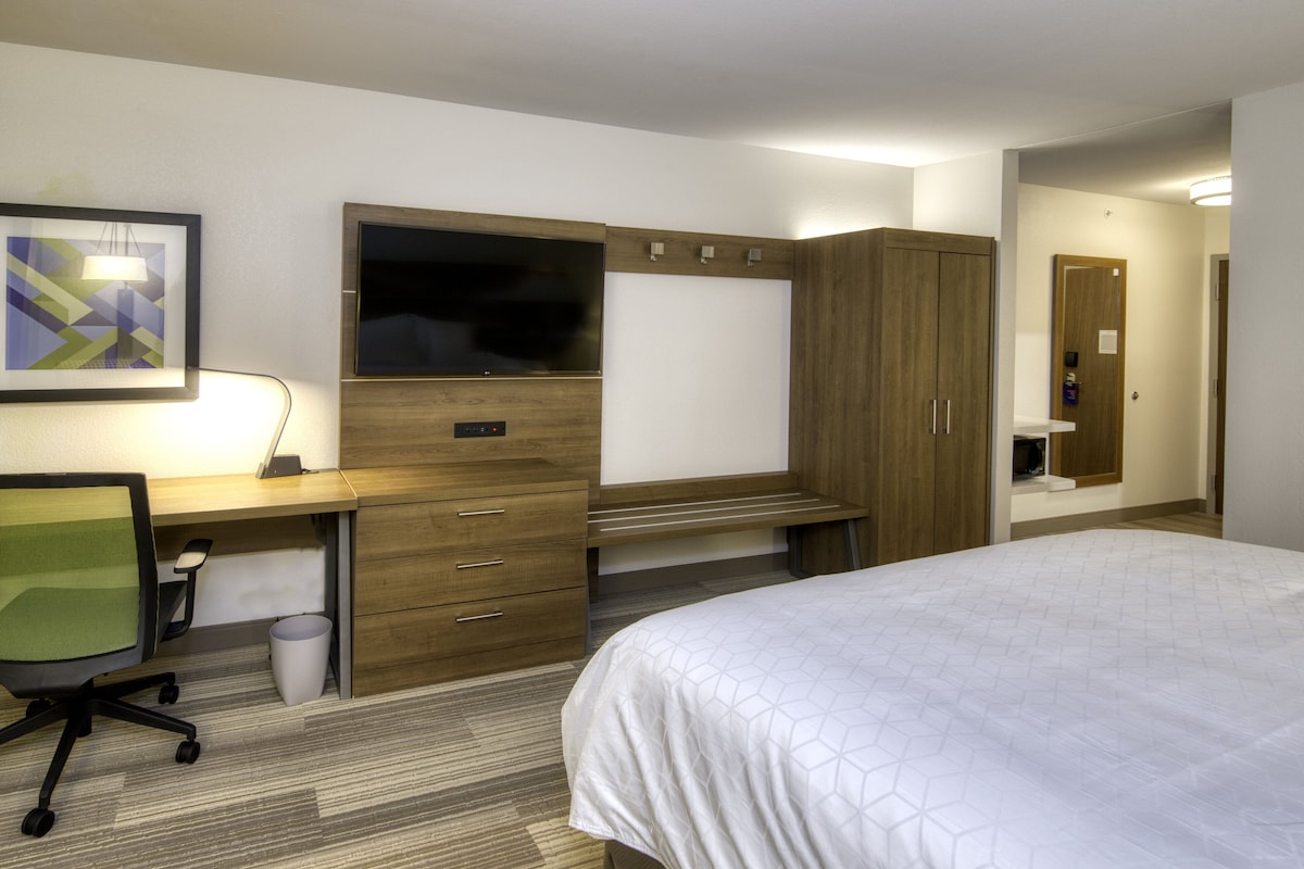 A hotel room with a bed, a desk with a chair, a TV, and a wardrobe.