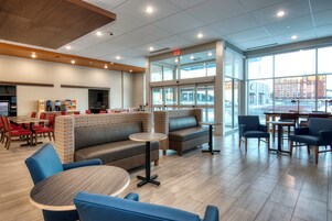 Un espace de détente intérieur moderne, avec un mélange de tables et de canapés, une grande fenêtre donnant sur la rue et un panneau de sortie bien visible.