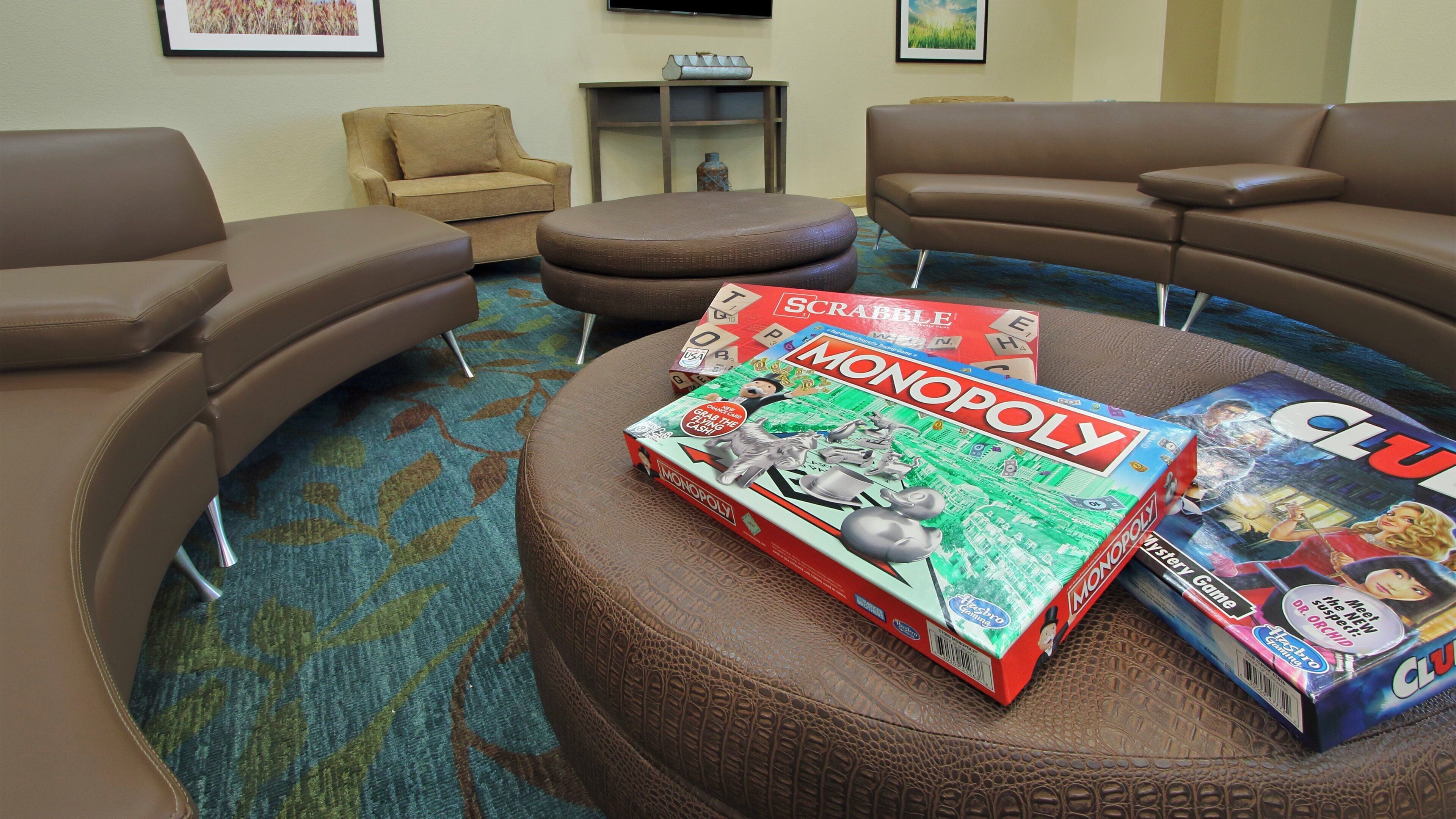 Una habitación con sofás de cuero marrón dispuestos en semicírculo, una mesa de centro con juegos de Monopoly y Scrabble, y una alfombra estampada.