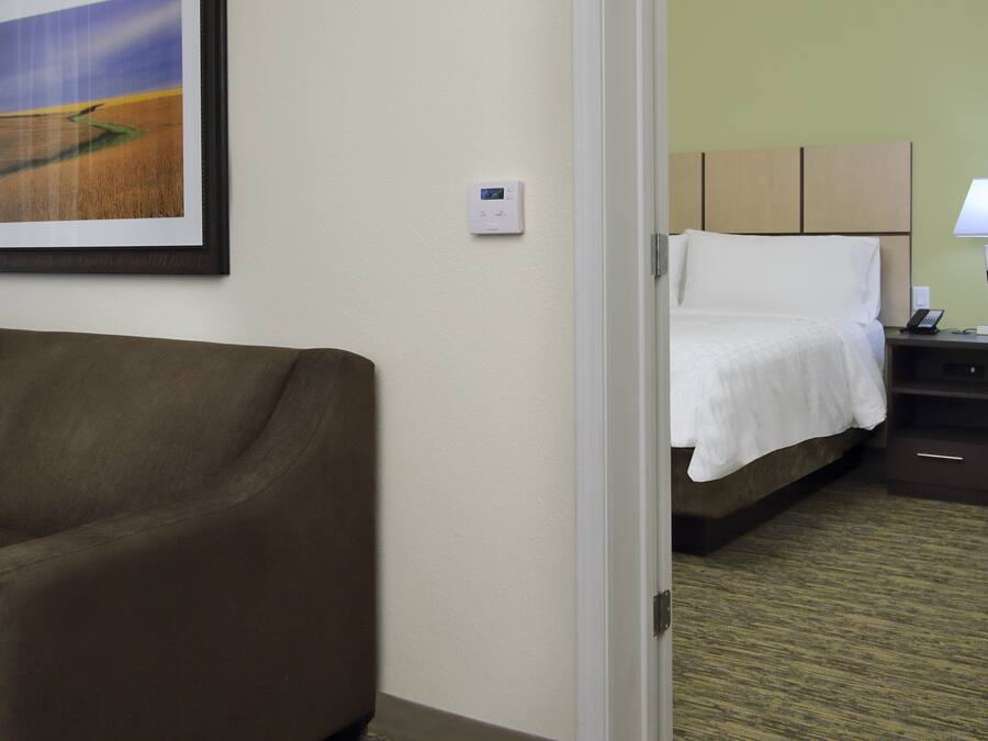 Une chambre d’hôtel avec un canapé marron, un lit avec du linge de lit blanc, une table de chevet avec une lampe et un tableau encadré au mur.