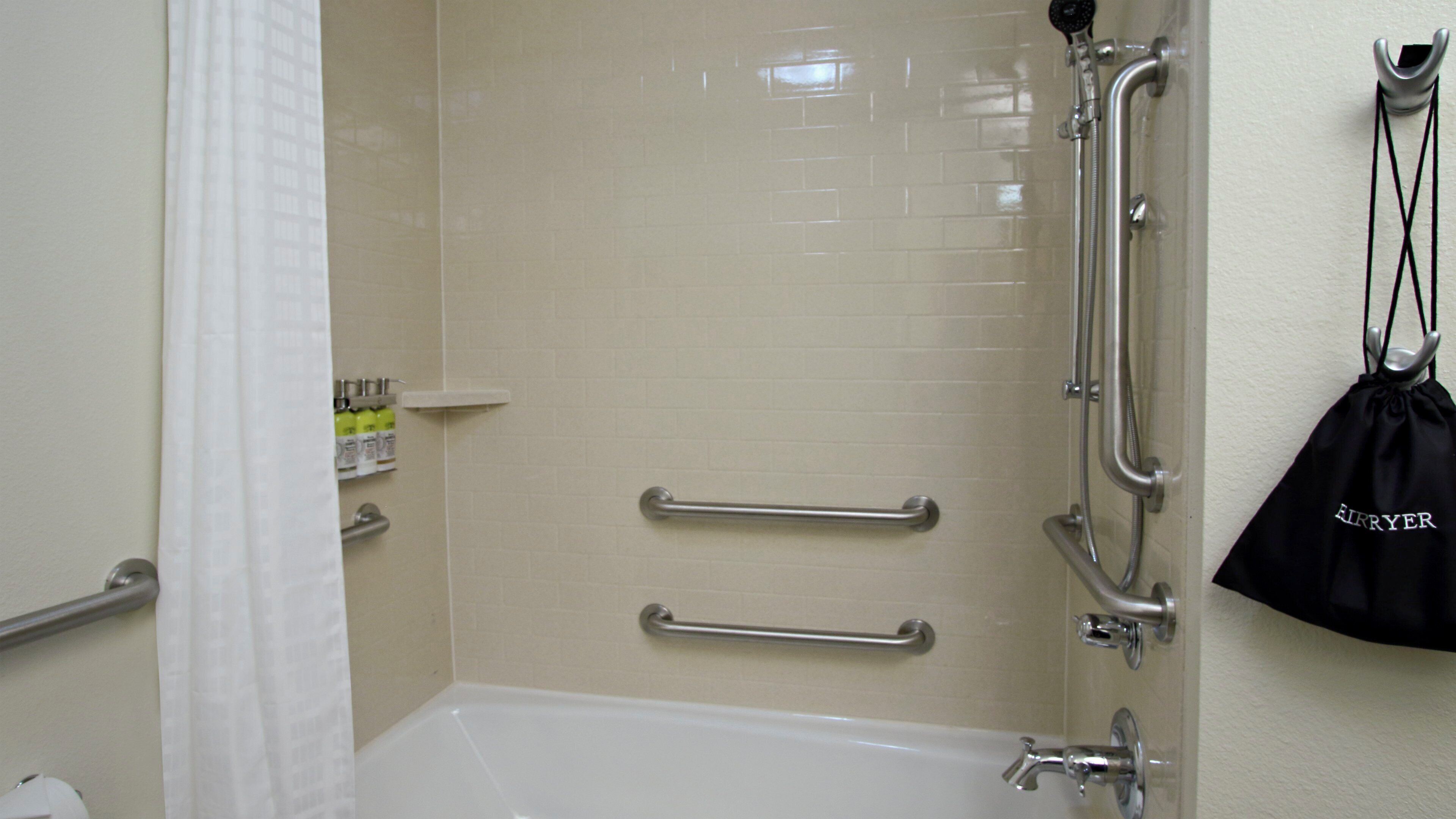A bathroom with a bathtub, grab bars, and a shower head.
