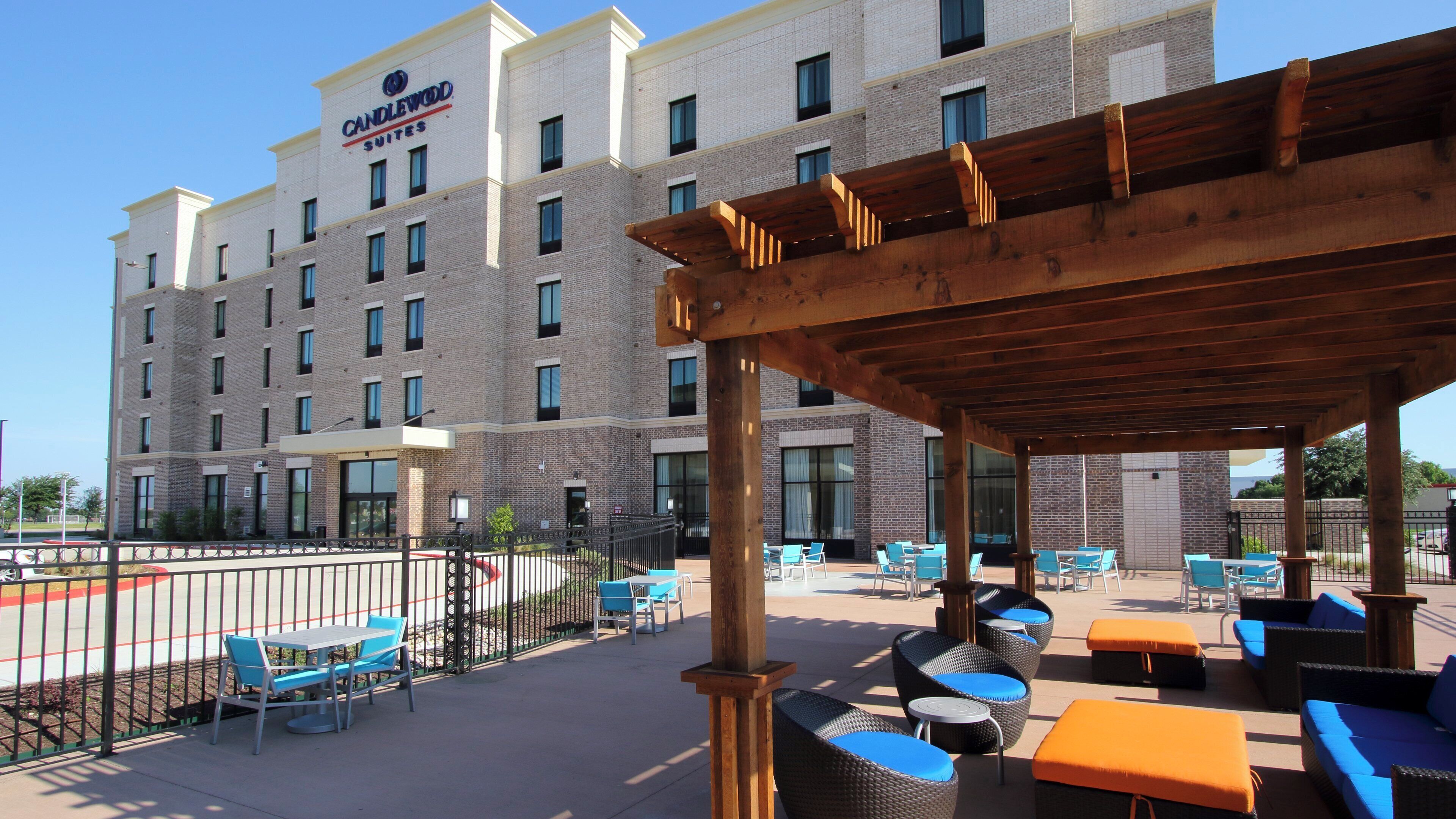 A hotel with a brick facade, outdoor seating area with wicker furniture, and a clear sky.