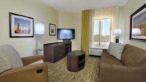 Une chambre d’hôtel équipée d’un téléviseur à écran plat, d’un canapé, d’un fauteuil, d’une petite table et d’une fenêtre avec des rideaux.