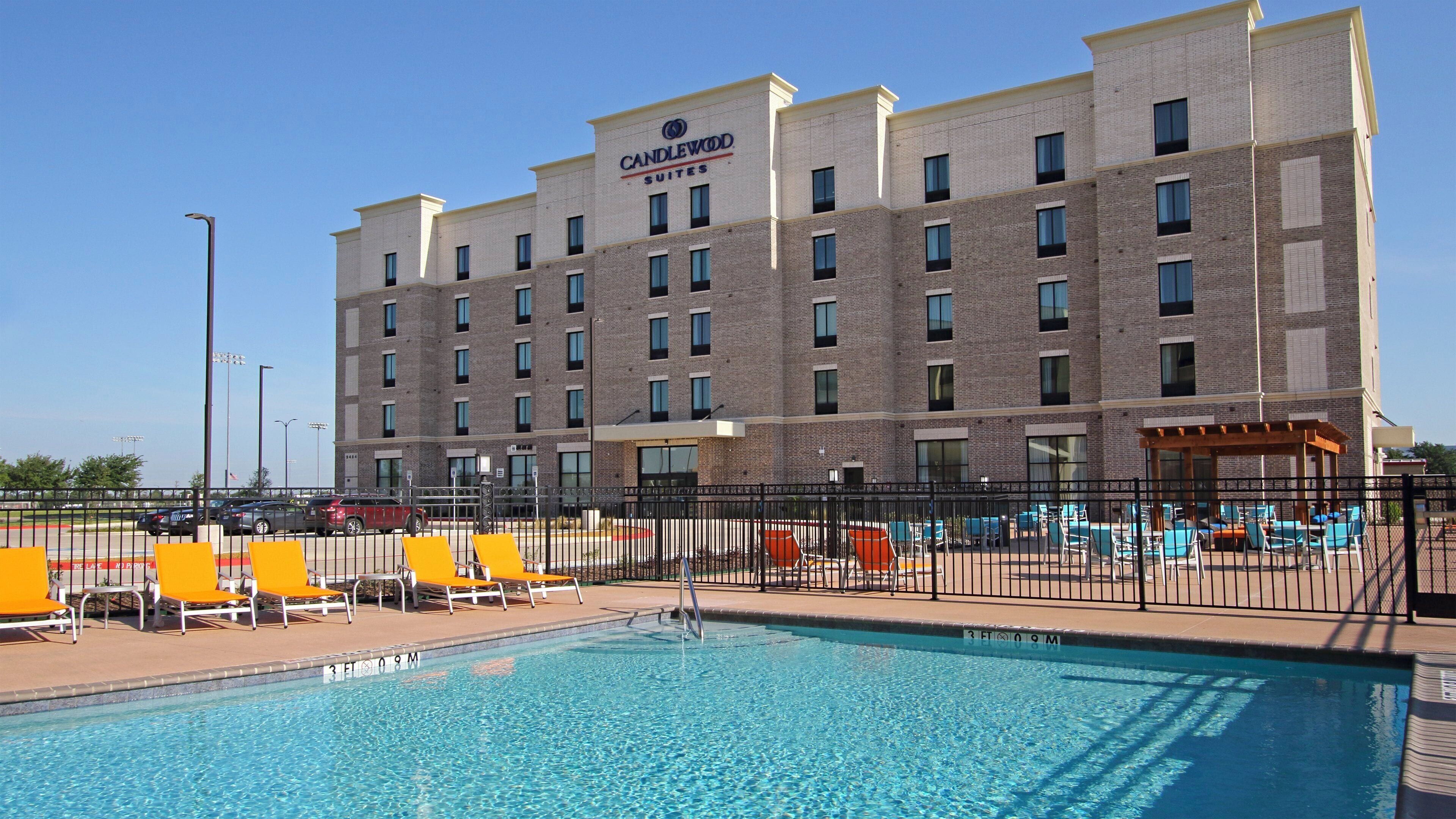 A hotel with a swimming pool, outdoor seating, and a clear sky.