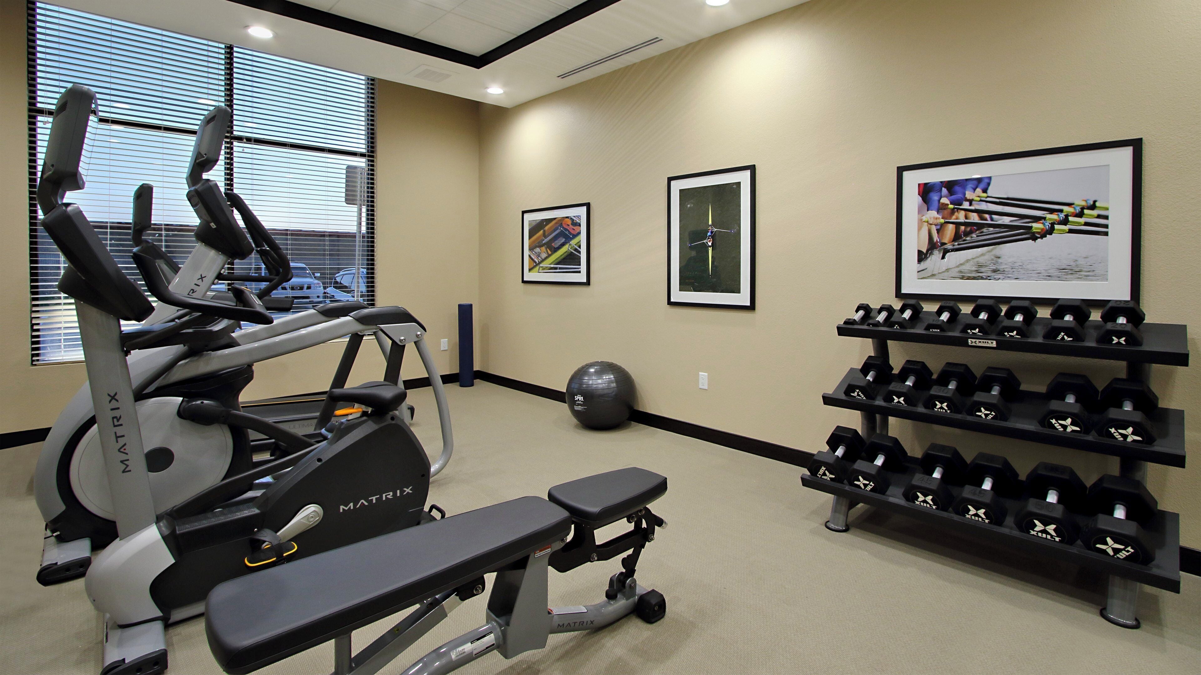 A gym with exercise equipment, dumbbells, and framed pictures on the walls.