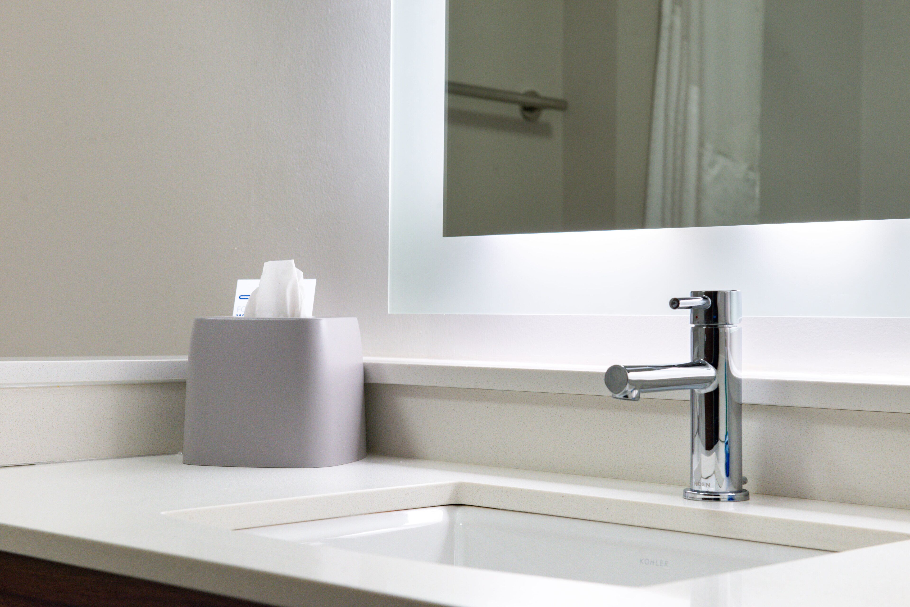 Un lavabo amb aixeta cromada, suport de mocadors i un mirall a la part superior.