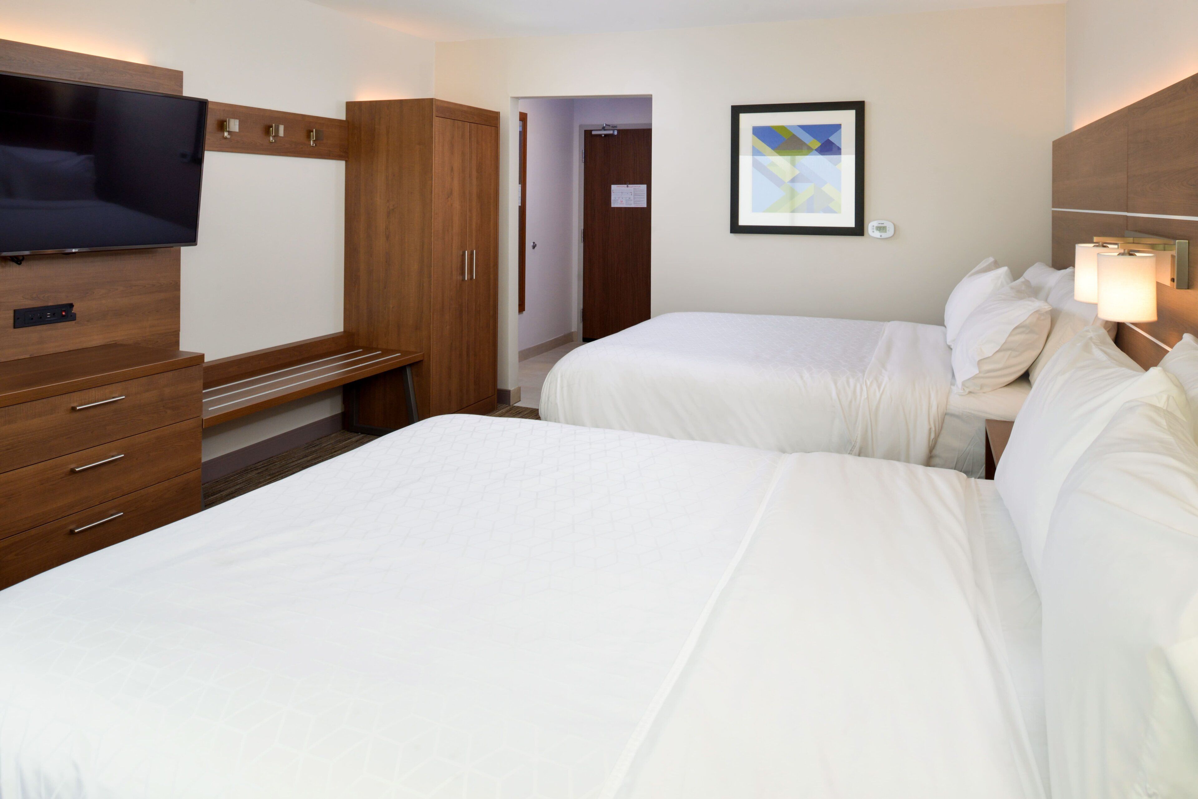 A hotel room with two beds, a TV, a wardrobe, and a framed picture on the wall.