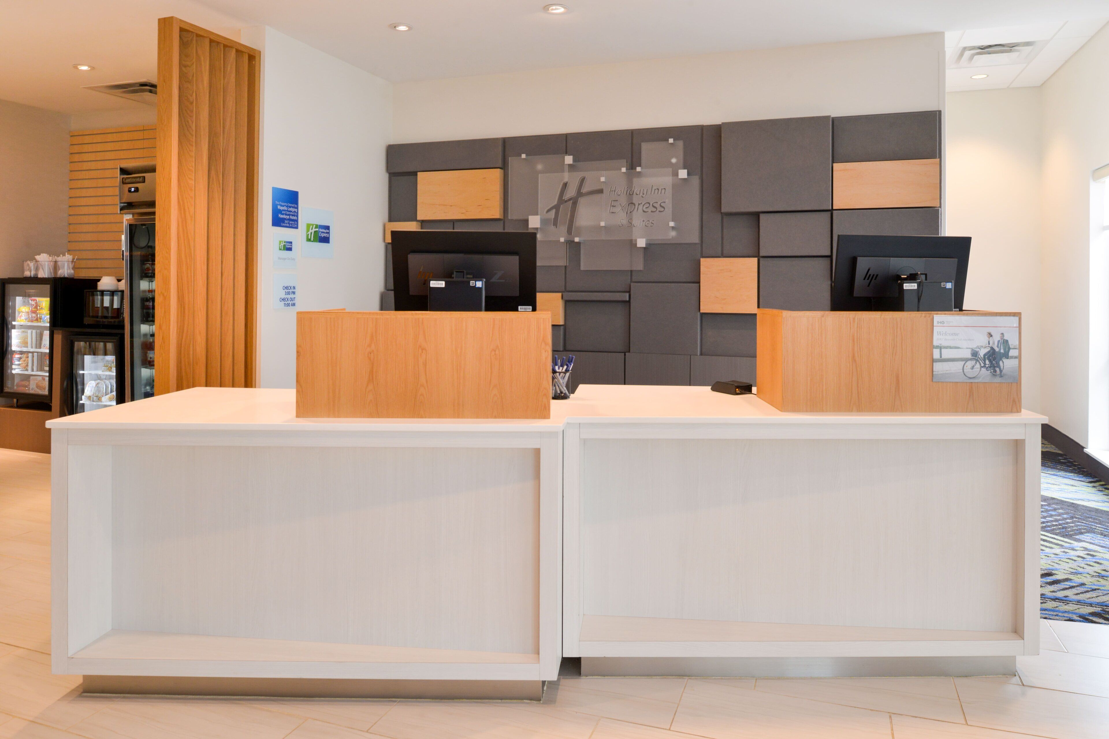 A hotel reception desk with a modern design, featuring a wooden reception counter and a grey wall with a geometric pattern.