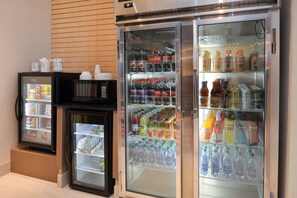 Máquina expendedora con diferentes snacks y bebidas, un microondas y un refrigerador lleno de refrescos.