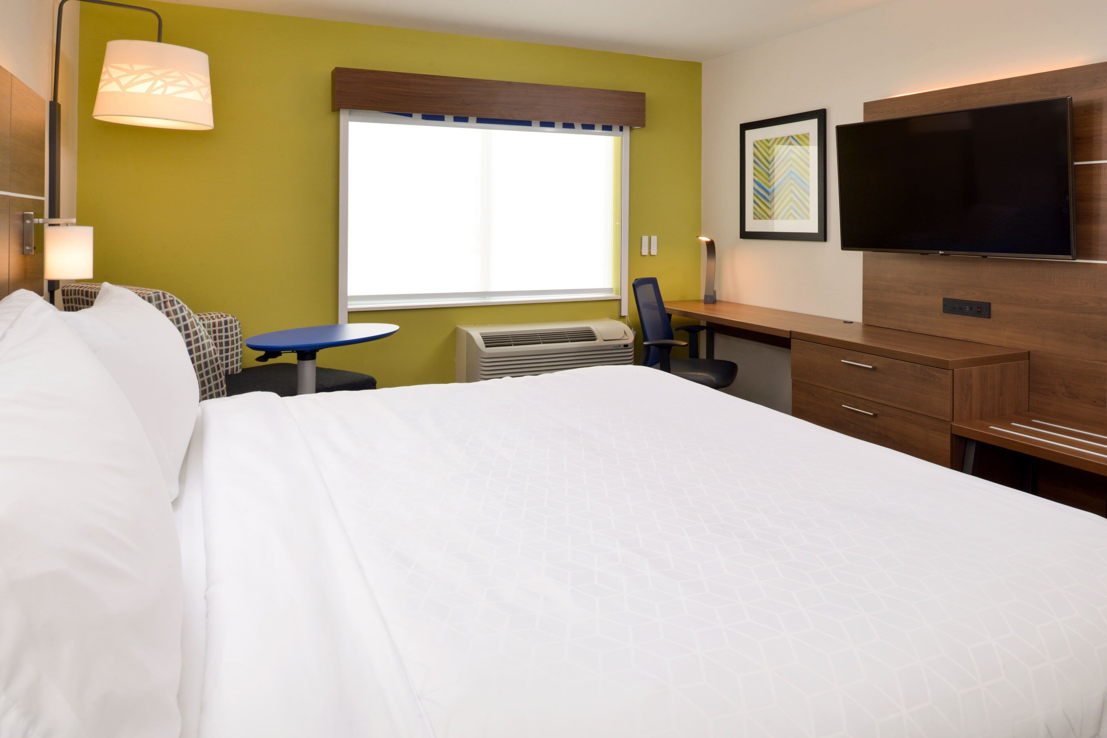 A hotel room with a large bed, a desk, a chair, a television, and a window with blinds.