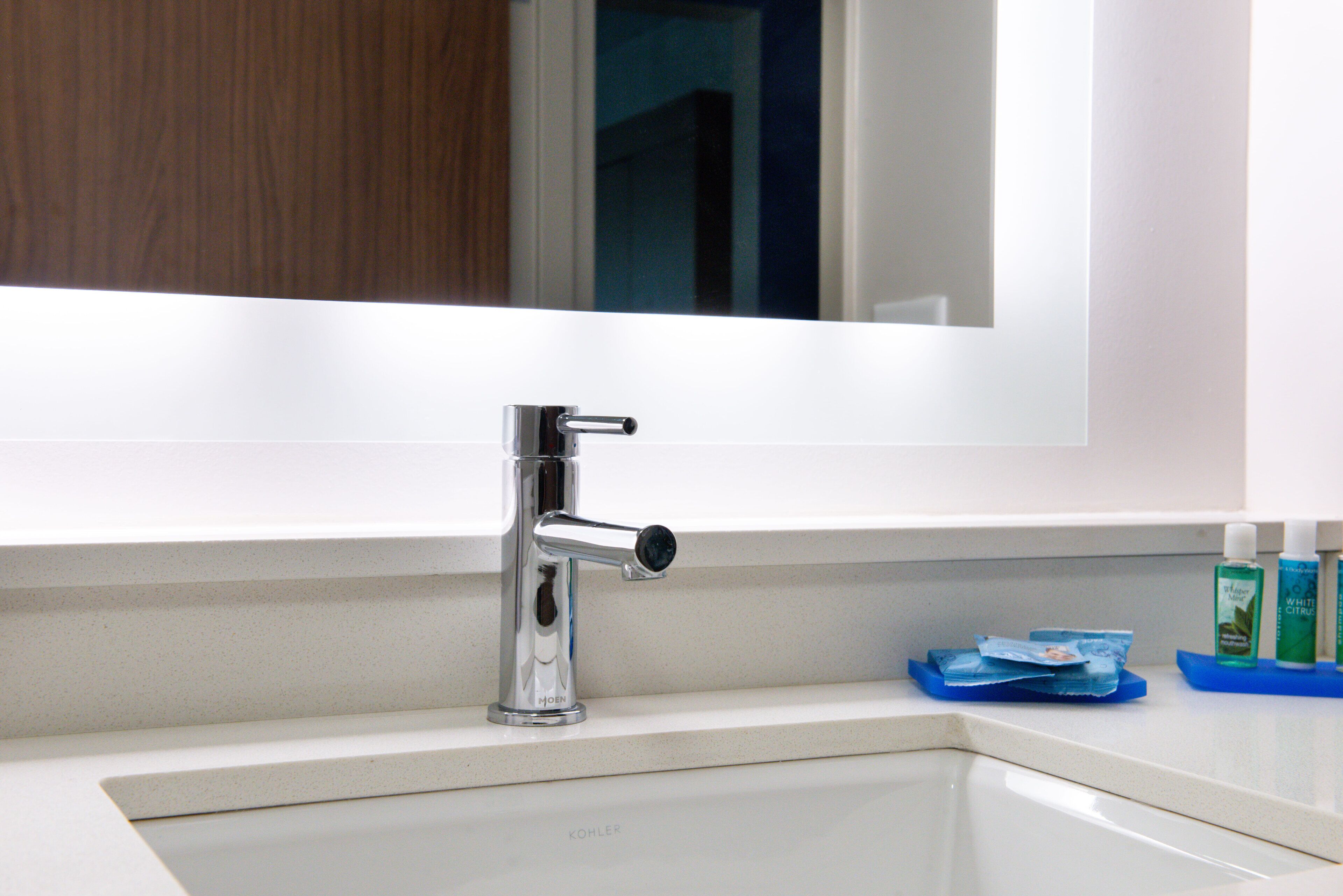A modern bathroom with a chrome faucet, a white sink, and a mirror above it.