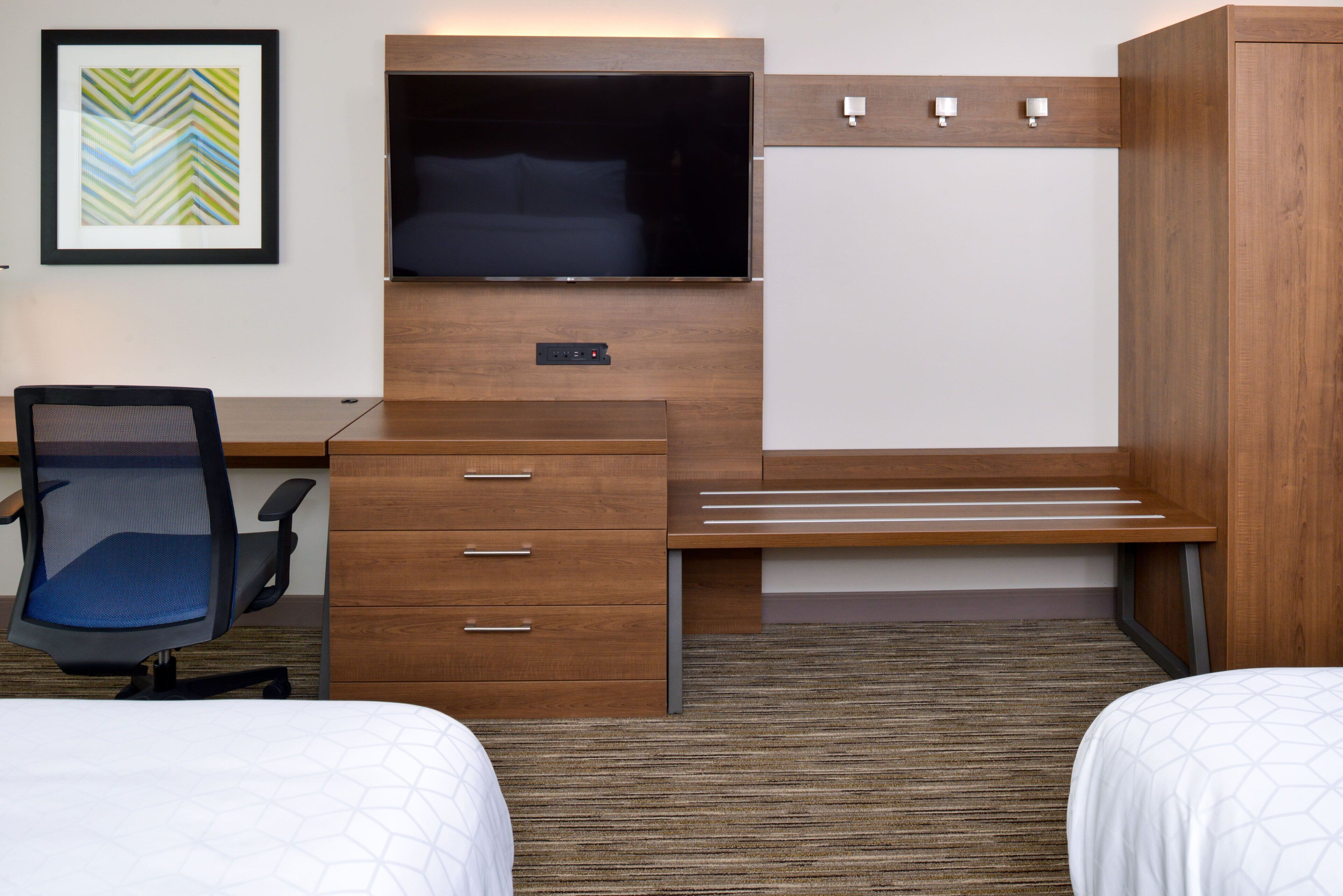 A hotel room with a bed, a desk with a chair, a TV, and a wardrobe.