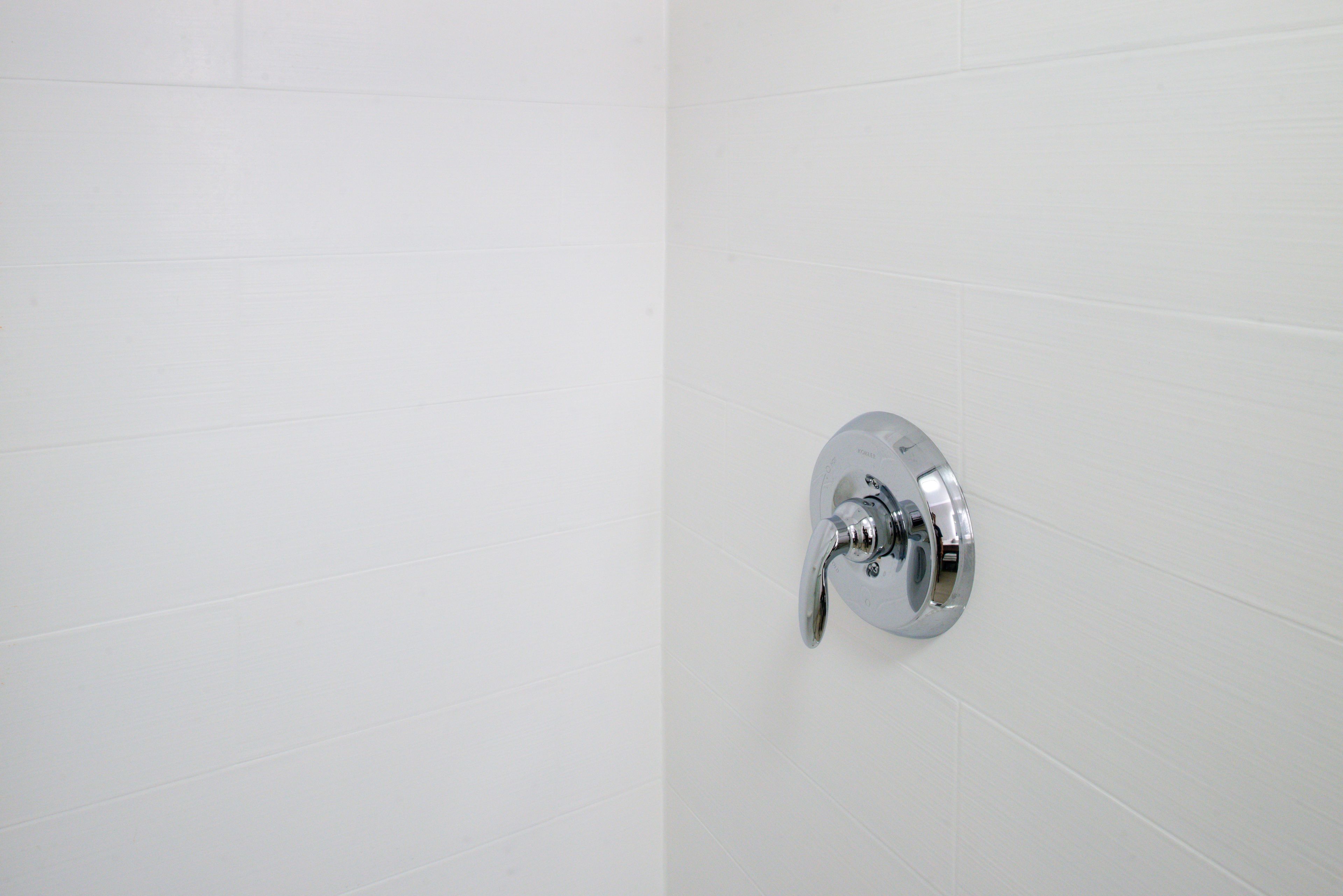 Un baño con paredes de azulejos blancos y un grifo cromado.