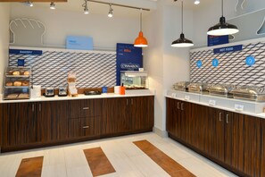 A bakery and hot food counter with wooden cabinets and a patterned wall. - Holiday Inn Express & Suites Ottumwa by IHG (Ottumwa)