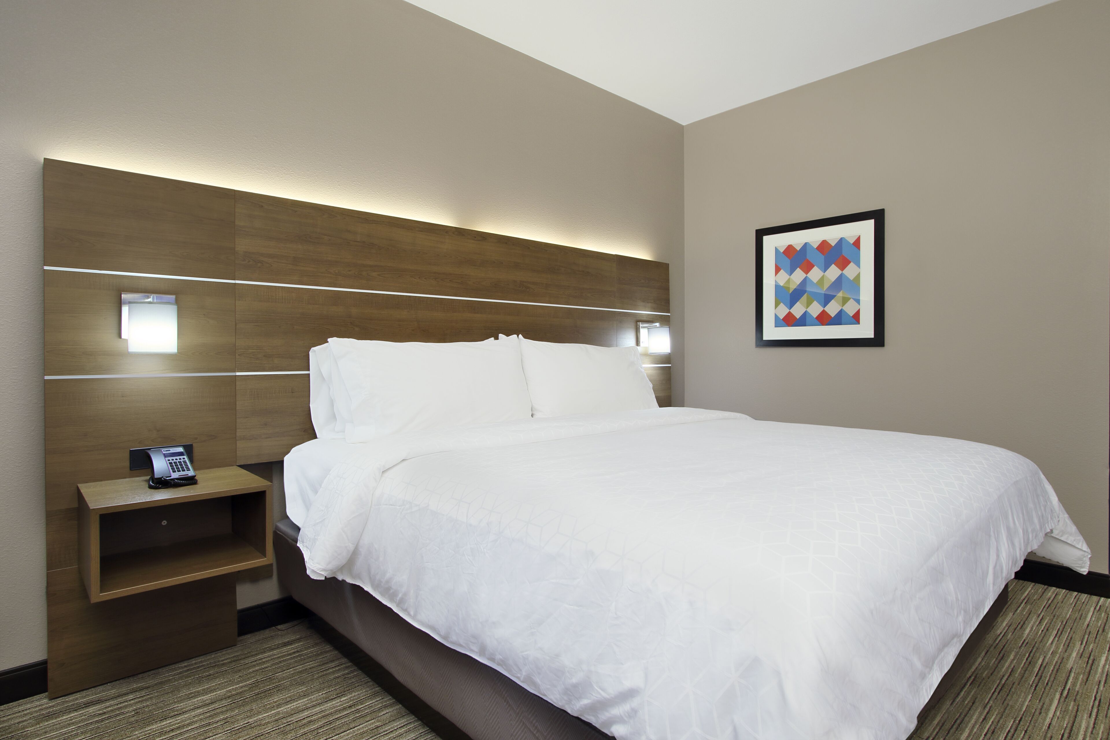 A hotel room with a large bed, a bedside table with a phone, and a wall-mounted light.