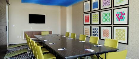 Uma sala de conferências com uma mesa comprida, cadeiras amarelas e quadros nas paredes.