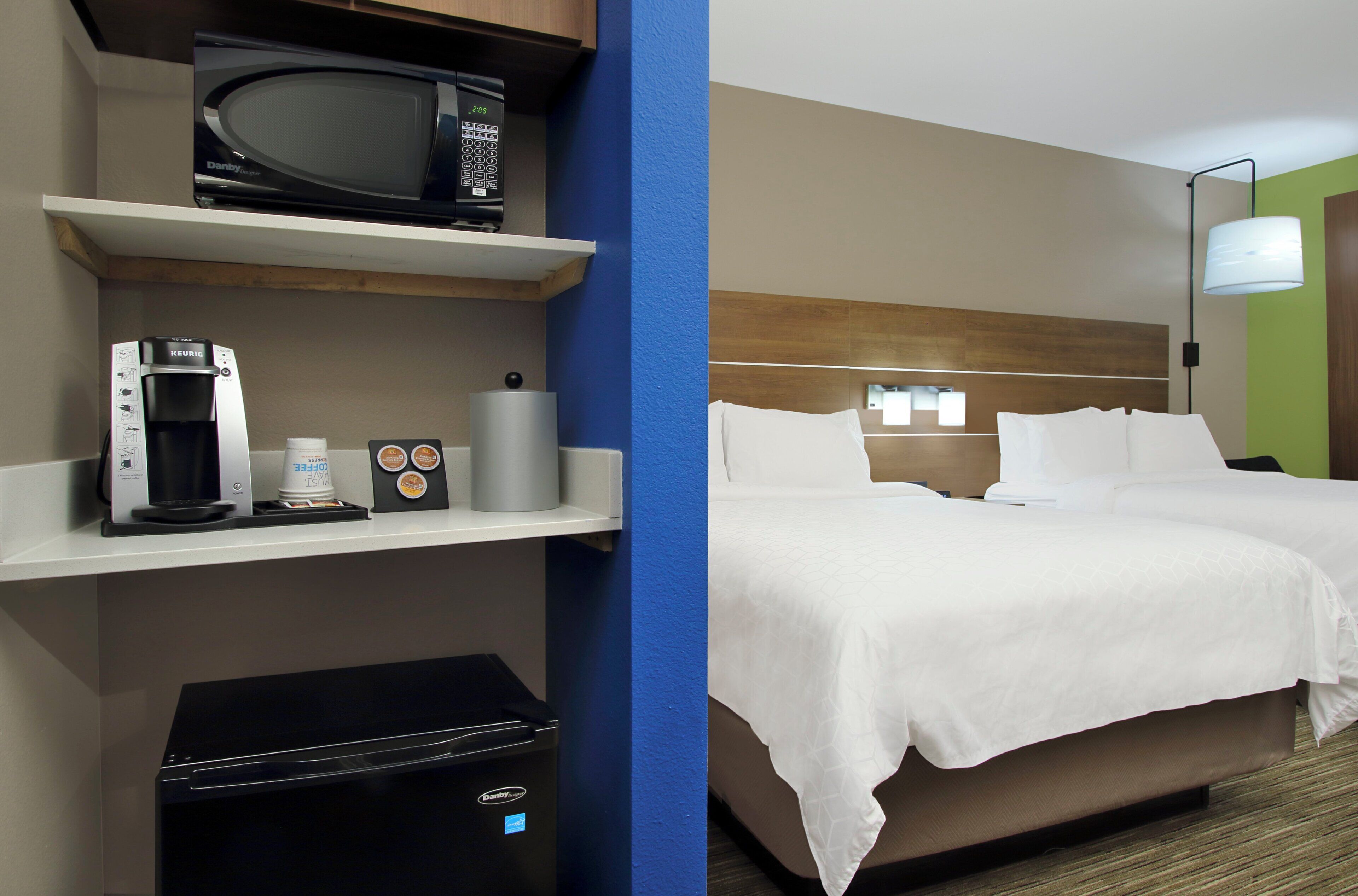 Een hotelkamer met een bed, een koffiezetapparaat, een magnetron en een prullenbak.