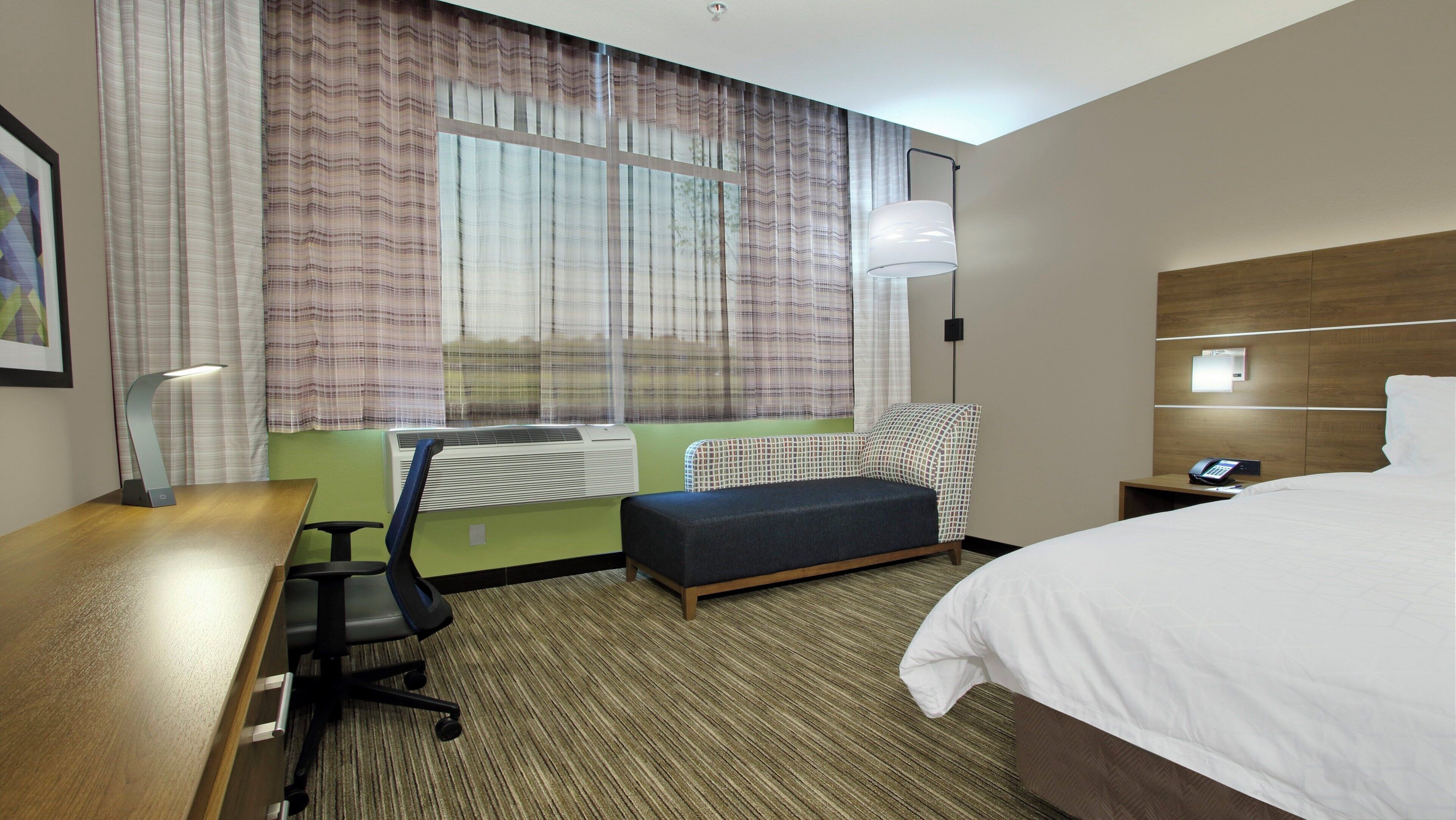 A hotel room with a bed, desk, chair, and a window with curtains.